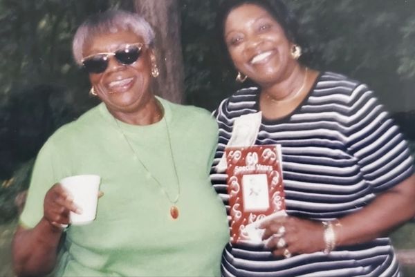 Two smiling women enjoying a moment outdoors, one holding a cup and the other holding a gift box.