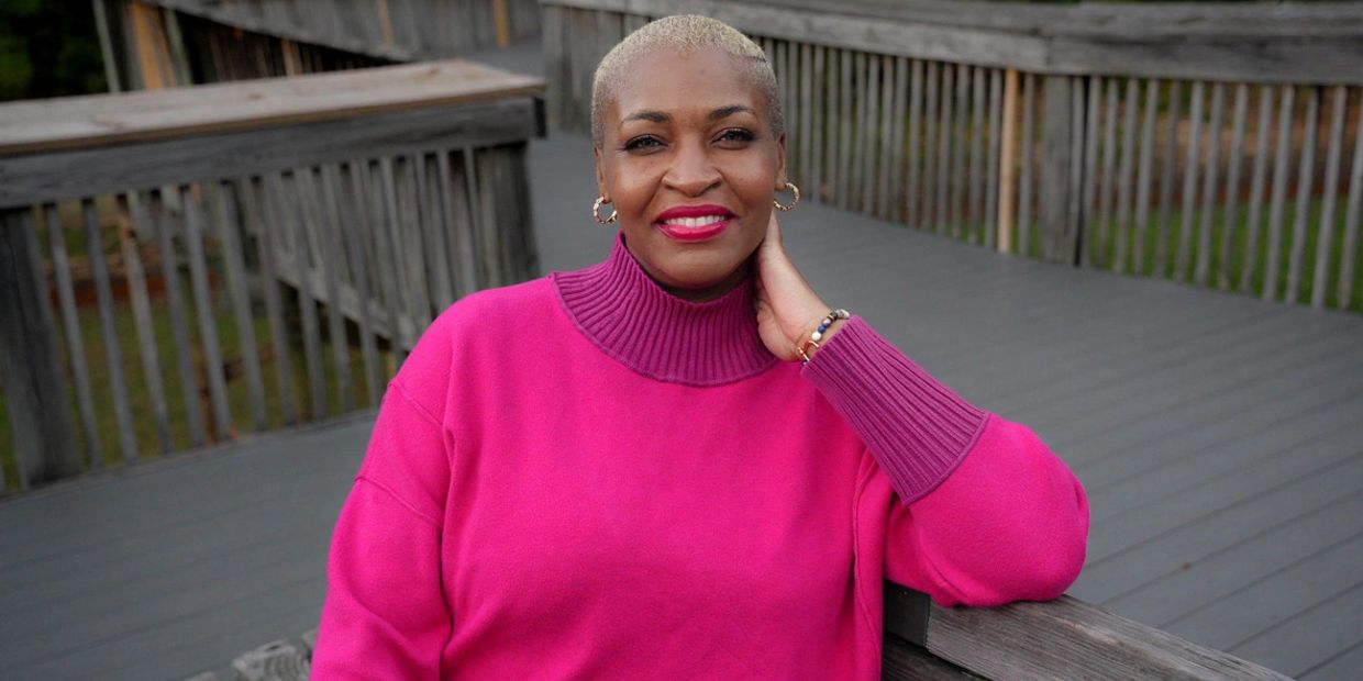 Founder and CEO, Solunis Nicole Bay, on a dock sitting on a wooden bench wearing a warm pink sweater.