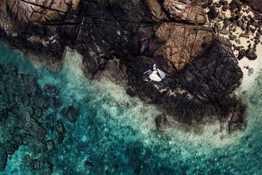 Aerial view of love — the couple lying on a seaside rock, surrounded by turquoise water and coral be