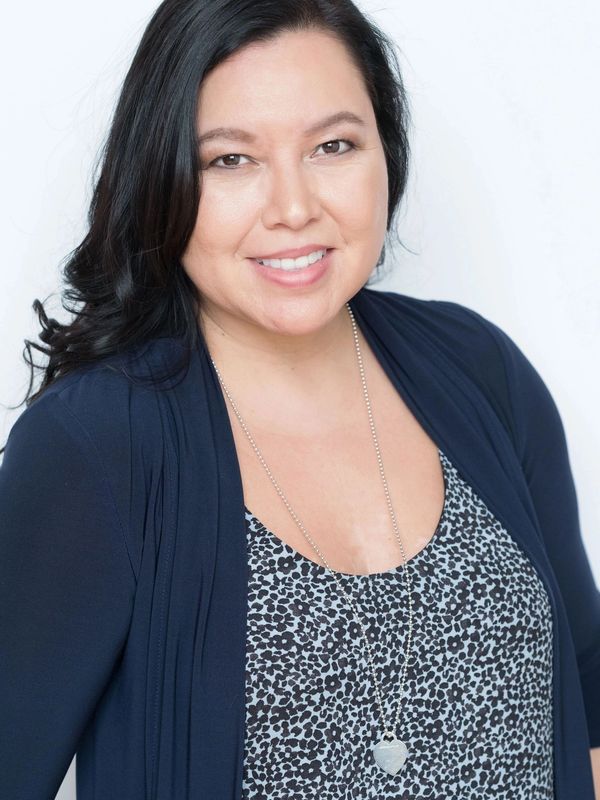 Smiling woman with dark hair wearing a floral top and navy cardigan.