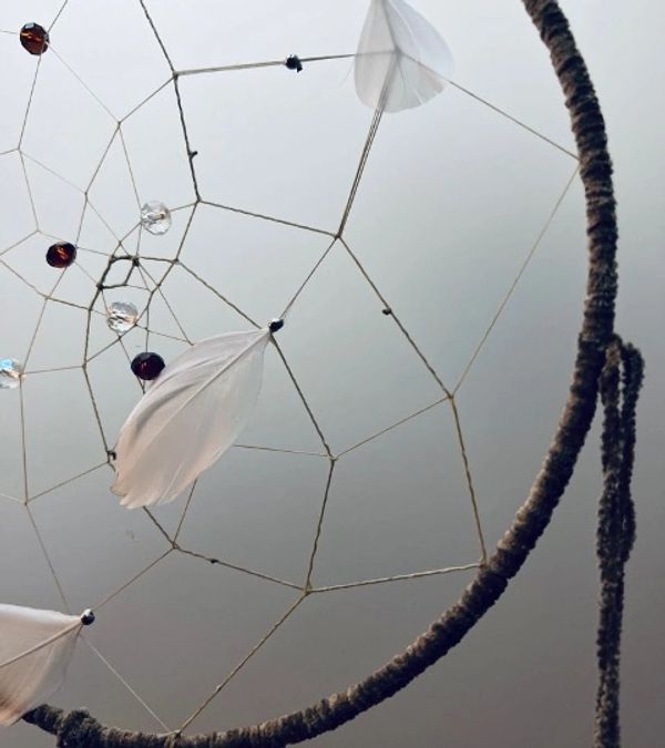 Close-up of a dreamcatcher with white feathers and beads.