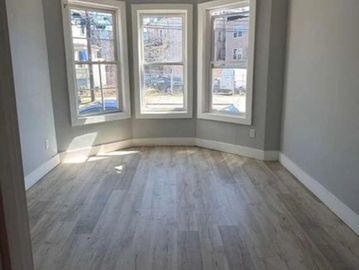 Empty room with light wood flooring and three large windows.