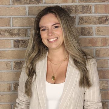 Smiling woman in a striped blazer posing against a brick wall.