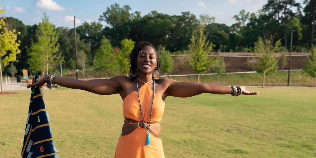 Dr. Makeba with arms lifted to the sides on a grassy field