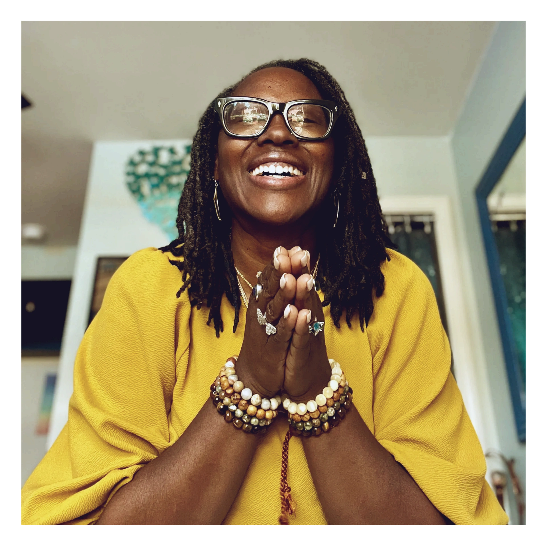 Dr. Makeba joyfully smiles with a gold shirt with hands in a prayer position.