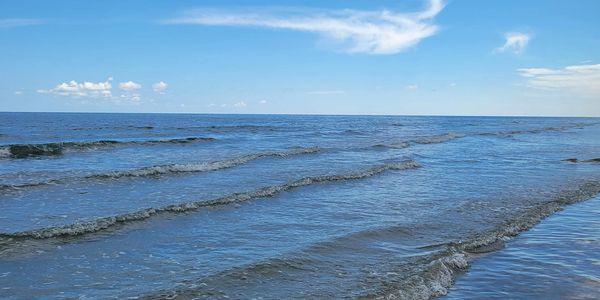 Beautiful blue skies with wisps of white clouds over ocean waves approaching the shore.