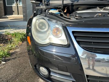 Front of a black Volkswagen with open hood and foggy headlight.