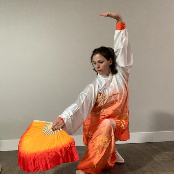 Woman performing traditional fan dance in orange and white attire.