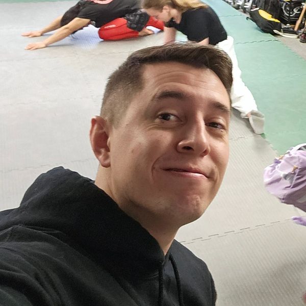 Man smiling in a gym with people stretching in the background.