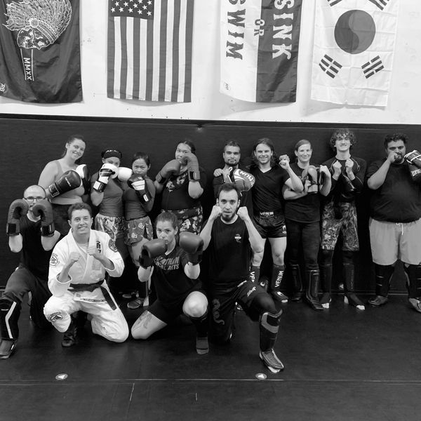 A group of martial artists posing with boxing gloves and protective gear in a training studio.