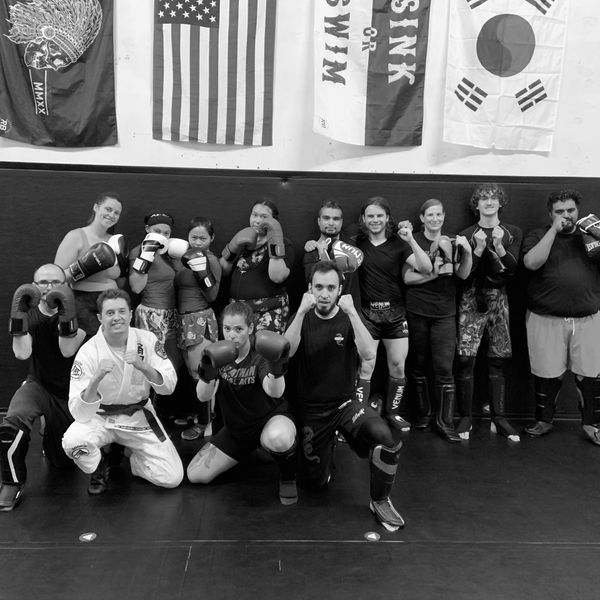 A group of martial artists posing with boxing gloves and protective gear in a training studio.