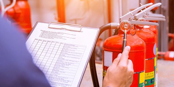 Person inspecting fire extinguishers with a checklist.