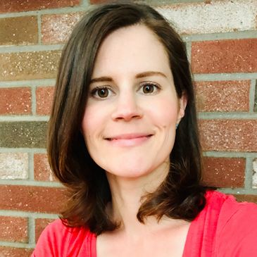 Woman with brown hair smiling against brick wall background.