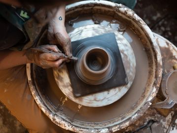 Potter making a handmade ceramic mug on the pottery wheel out of clay and glaze. 