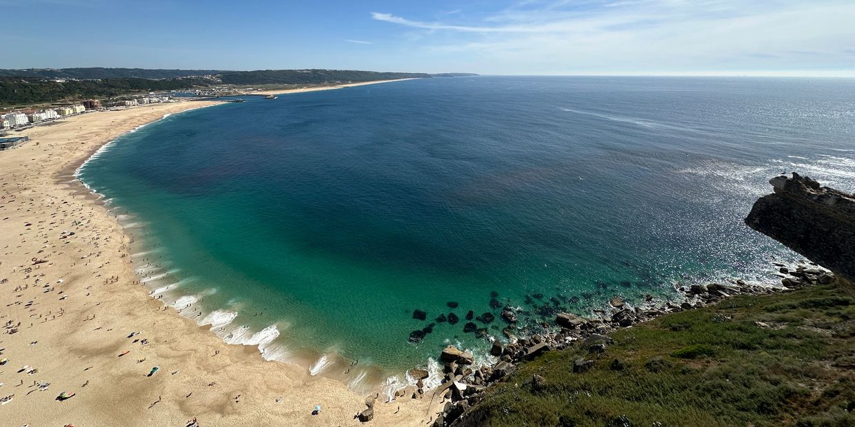 Panoramic view of a sunny beach with turquoise waters and rocky coastline.