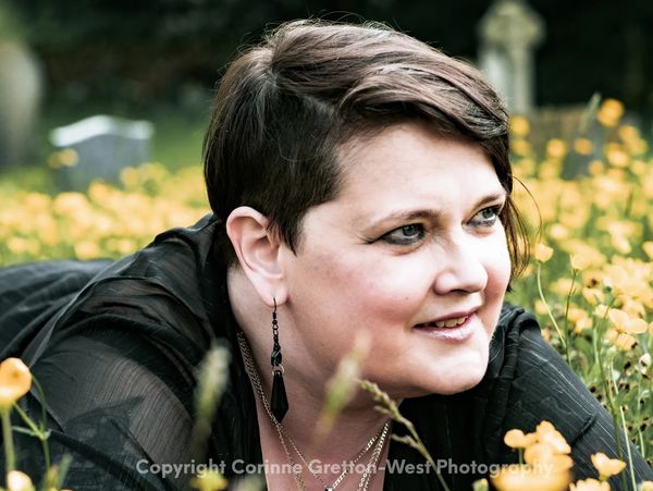 A lady with short dark hair, wearing black, lies in a field of buttercups.