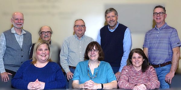 Group portrait of eight diverse adults smiling in a casual setting.