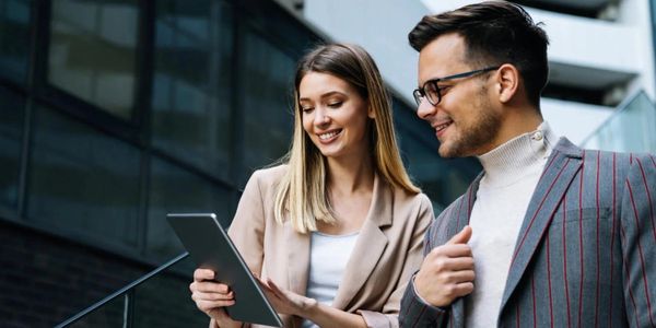 Two young professionals happily discussing work using a tablet outdoors.