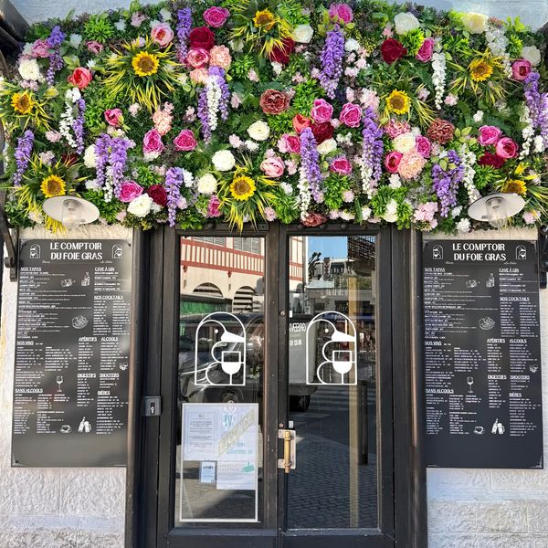 Entrance of a restaurant adorned with colorful flowers and menus on both sides.