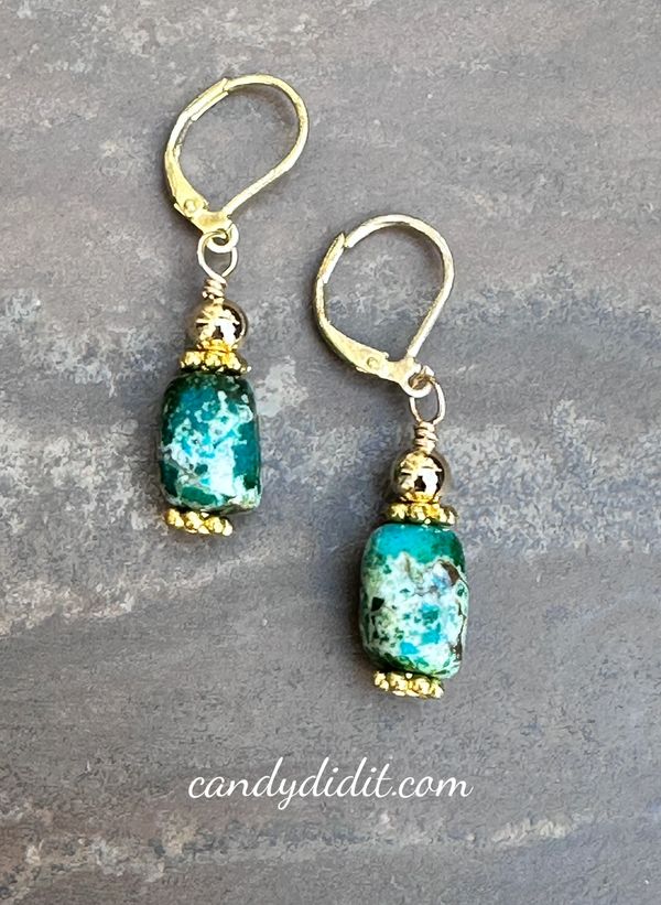 Gold and teal gemstone drop earrings on a stone surface.