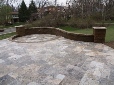 Curved stone patio with low wall and grassy yard.