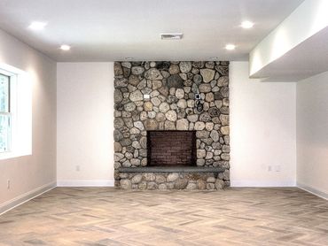 Rustic river rock fireplace in a clean, white, unfinished basement room.
