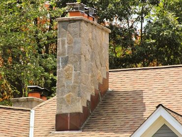 Chimney covered in flat stone veneer rising above a shingle roof.
