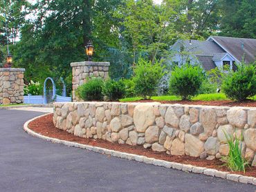 Stone retaining wall with bushes in a residential setting.
