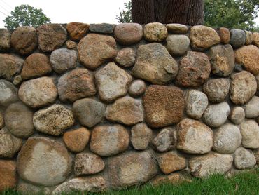 Section of curved river rock wall with green grass.