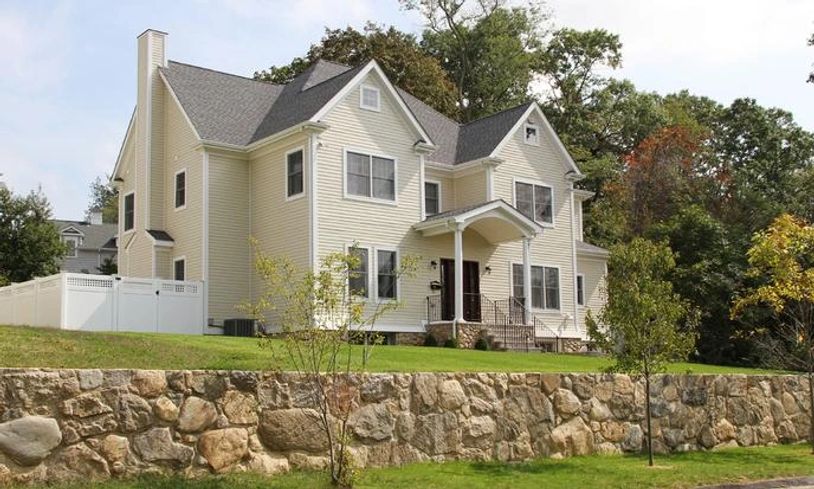 Front exterior of a light beige two-story house with a prominent chimney, behind a large stone