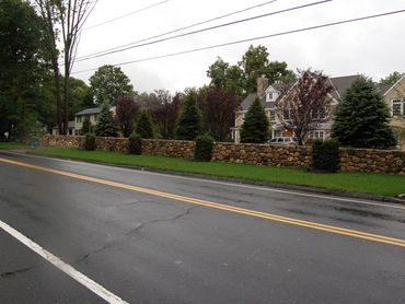 Stone wall bordering a paved road or driveway.

