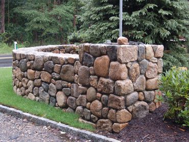 Corner view of a dark, rustic stone retaining wall.
