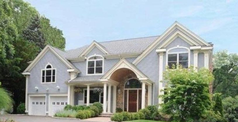 Front exterior of a large, light blue or gray house with white trim, an arched entryway

