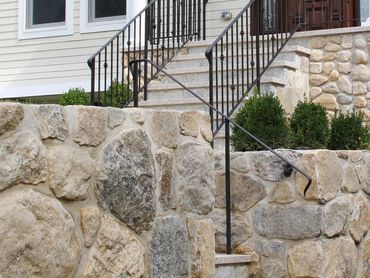 Low, rough-cut stone wall section near a house.
