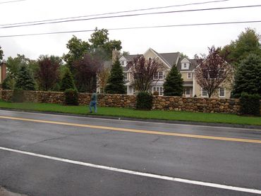 Stone wall and landscaping along a paved road.
