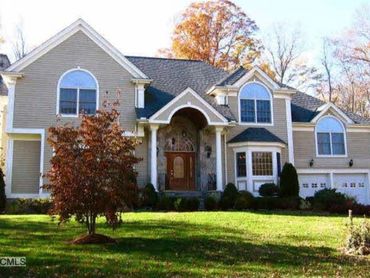 Full view of a light-colored house with stone accents and a fall landscape.
