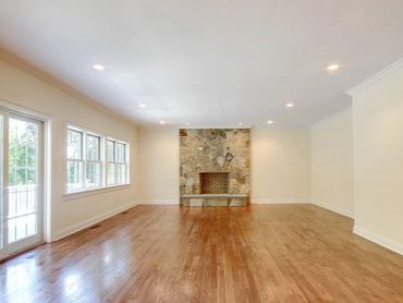 Stone fireplace centered in a large, empty room with wood flooring.
