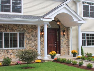 Home entryway with light siding, columns, and a dark front door.
