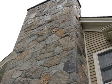 Exterior view of a chimney covered with large, flat, variegated stone veneer.
