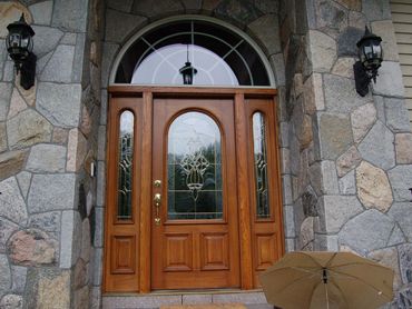 Large arched entry with wood door and stone siding, with decorative lights.

