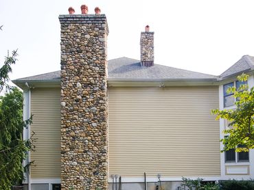 Side view of a beige house featuring a tall, stacked stone chimney.

