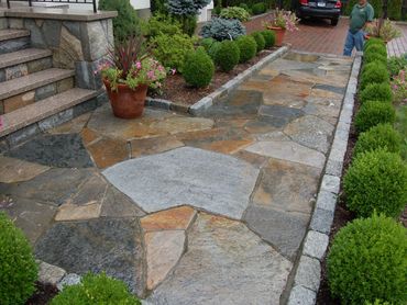 Irregular flagstone patio or walkway bordered by a low hedge.
