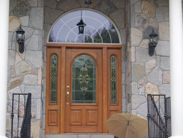 Arched wooden door with glass, surrounded by stone veneer and porch lights.
