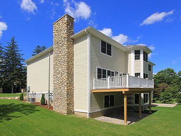 Exterior view of a tan house with a second-floor deck and stone chimney.
