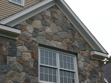 Close-up of a gable with stone siding and an arched transom window.
