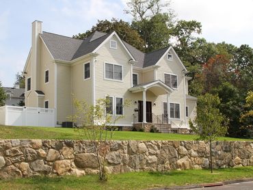 Stone retaining wall surrounding a grassy area near a house.
