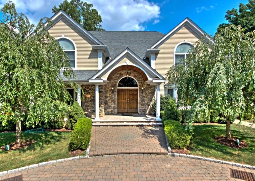 Front exterior of a large, beige house with a stone-accented entrance and a brick driveway.


