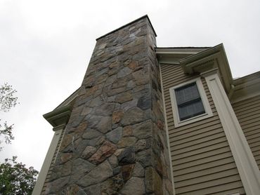 Low-angle view of a stone chimney column on a tan sided house.
