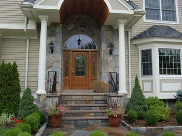 Entryway with stone steps, columns, and a natural wood door.
