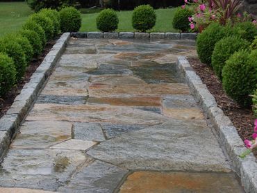 Stone flagstone path leading through manicured hedges and lawn.
